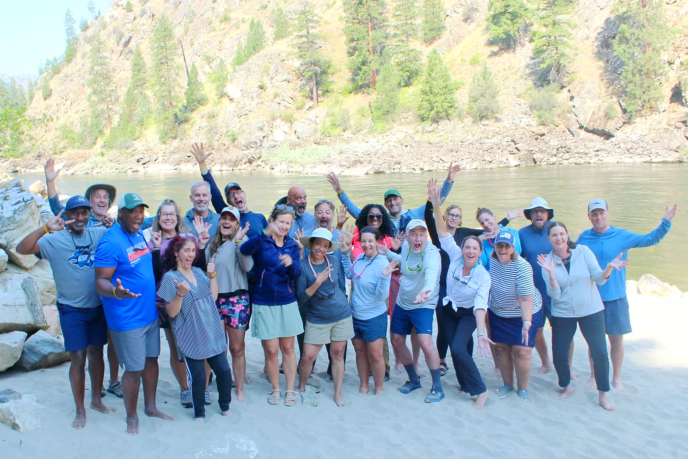 A large group of heads of school cheering on a sandy beach by the Salmon River