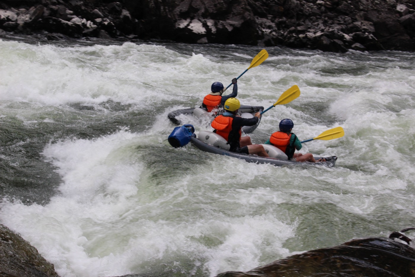 Three paddlers in an inflatable kayak running whitewater