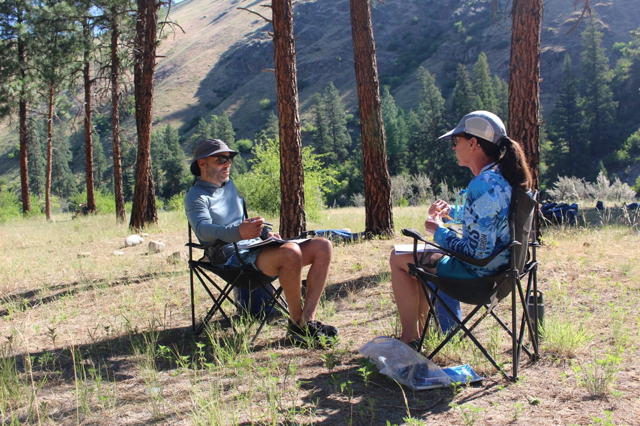 Two participants in camp chairs talking under the pines
